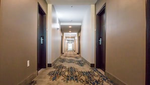 Un pasillo de hotel con pisos alfombrados, puertas a ambos lados y una fuente de luz al final.