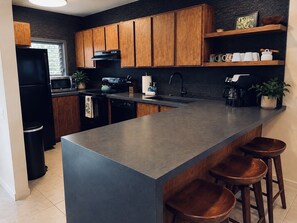 A modern kitchen with wooden cabinets, a large island, bar stools, and a coffee machine. - Kona Bali Kai 223 - Oceanfront 2 Bedroom Condo by RedAwning (Kailua-Kona)