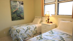 A bedroom with two single beds, a nightstand with a lamp, a clock, and a painting of a person swimming with a turtle. - Kona Bali Kai 223 - Oceanfront 2 Bedroom Condo by RedAwning (Kailua-Kona)