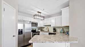 A modern kitchen with white cabinets, stainless steel appliances, a granite countertop, and a bar stool area. - Phoenix VII 71113 by ALBVR (Orange Beach)