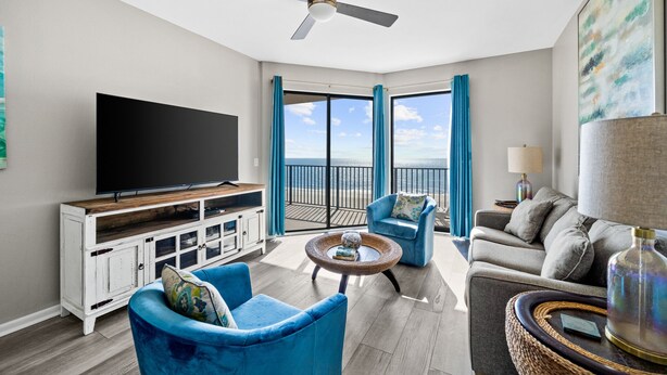 A modern living room with a flat-screen TV, blue armchairs, a grey sofa, and a balcony with a view of the ocean. - Phoenix VII 71113 by ALBVR (Orange Beach)