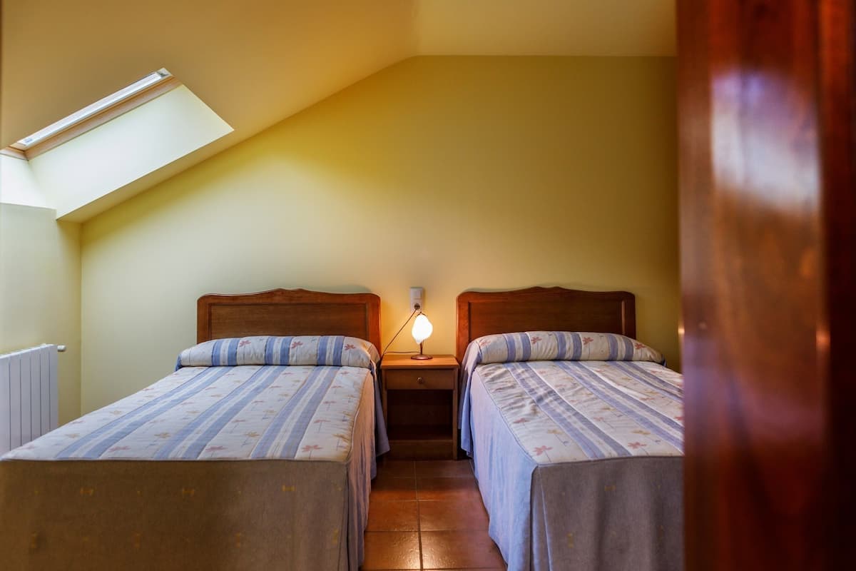 Una camera da letto accogliente e piccola con due letti singoli, un comodino con una lampada e un lucernario.
