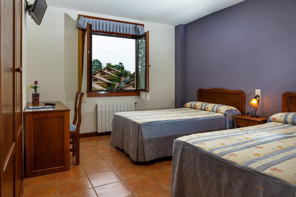 Una camera da letto con due letti, una finestra che dà su case, una scrivania con un vaso e una sedia.