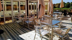 An outdoor dining area with tables and chairs, large windows, and umbrellas.