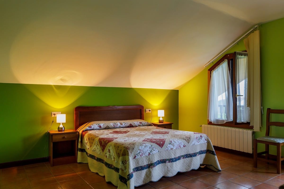 Una camera da letto con un letto, due abat-jour, una finestra con tende e un termosifone.