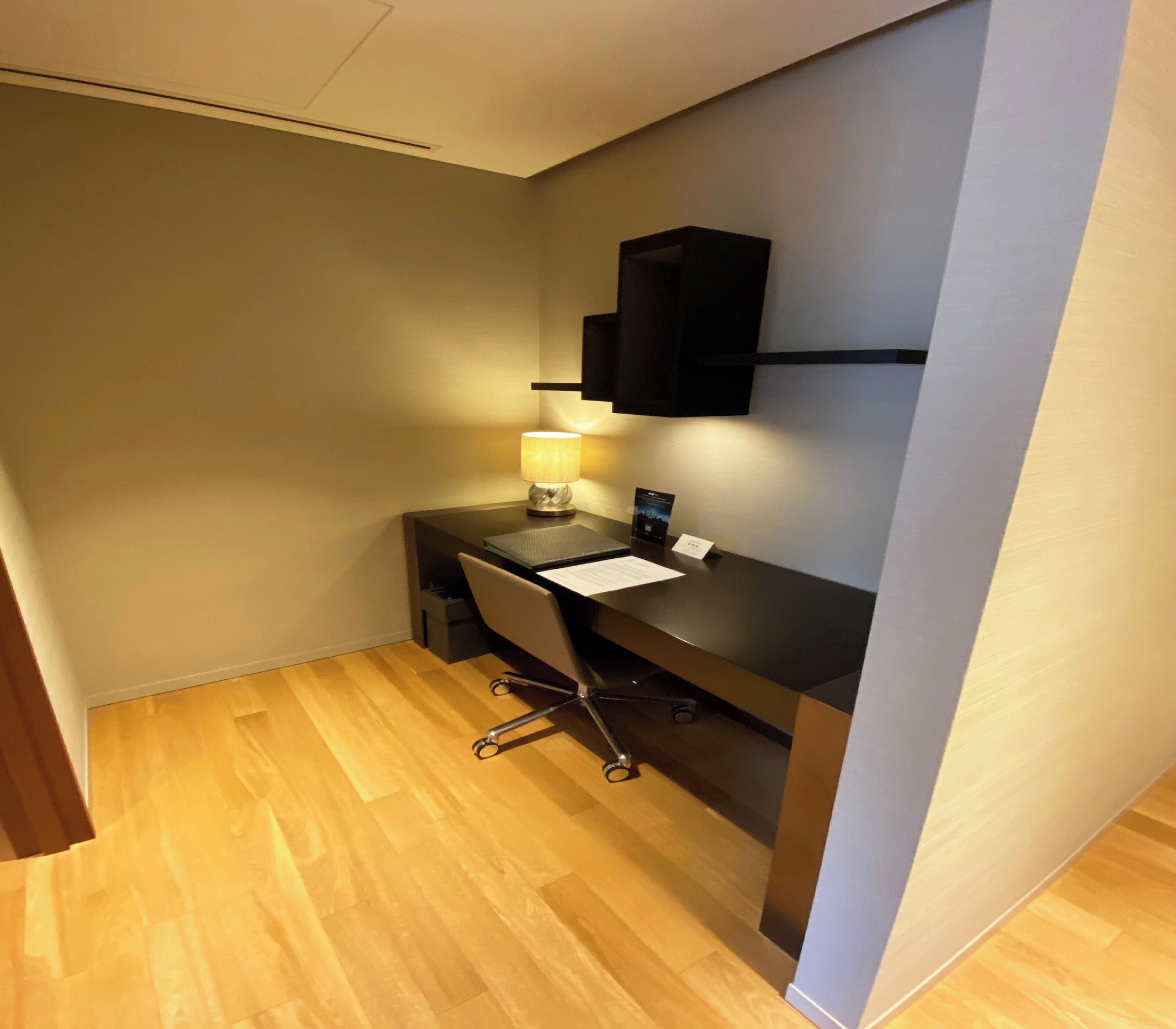 A small, modern office space with a desk, chair, lamp, and a black shelf unit.