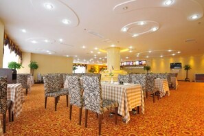 A hotel dining area with round tables, chairs, and a carpeted floor.