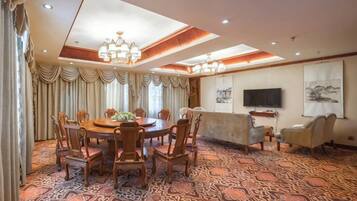 A hotel dining room with a round table, chairs, a sofa, and a television.