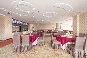 Un restaurante con mesas redondas, sillas y una pantalla de televisión.