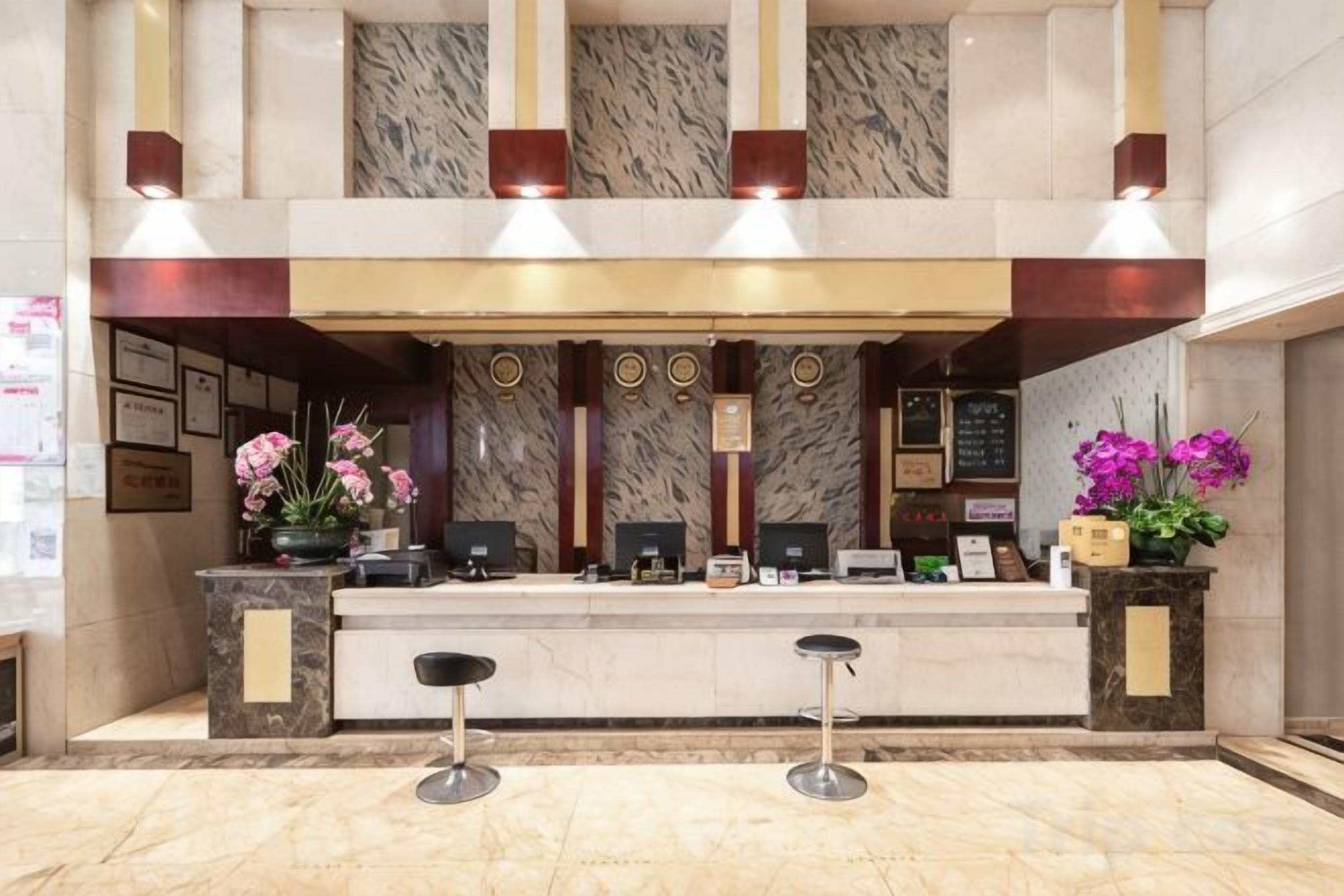 A hotel reception area with a marble counter, two bar stools, and decorative flowers.