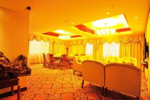 A hotel room with a large bed, a desk, and a chair. There is a window with curtains and a chandelier.