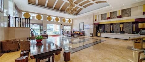 En rummelig lobby med højt til loftet, en reception og et siddeområde med et bord og stole.