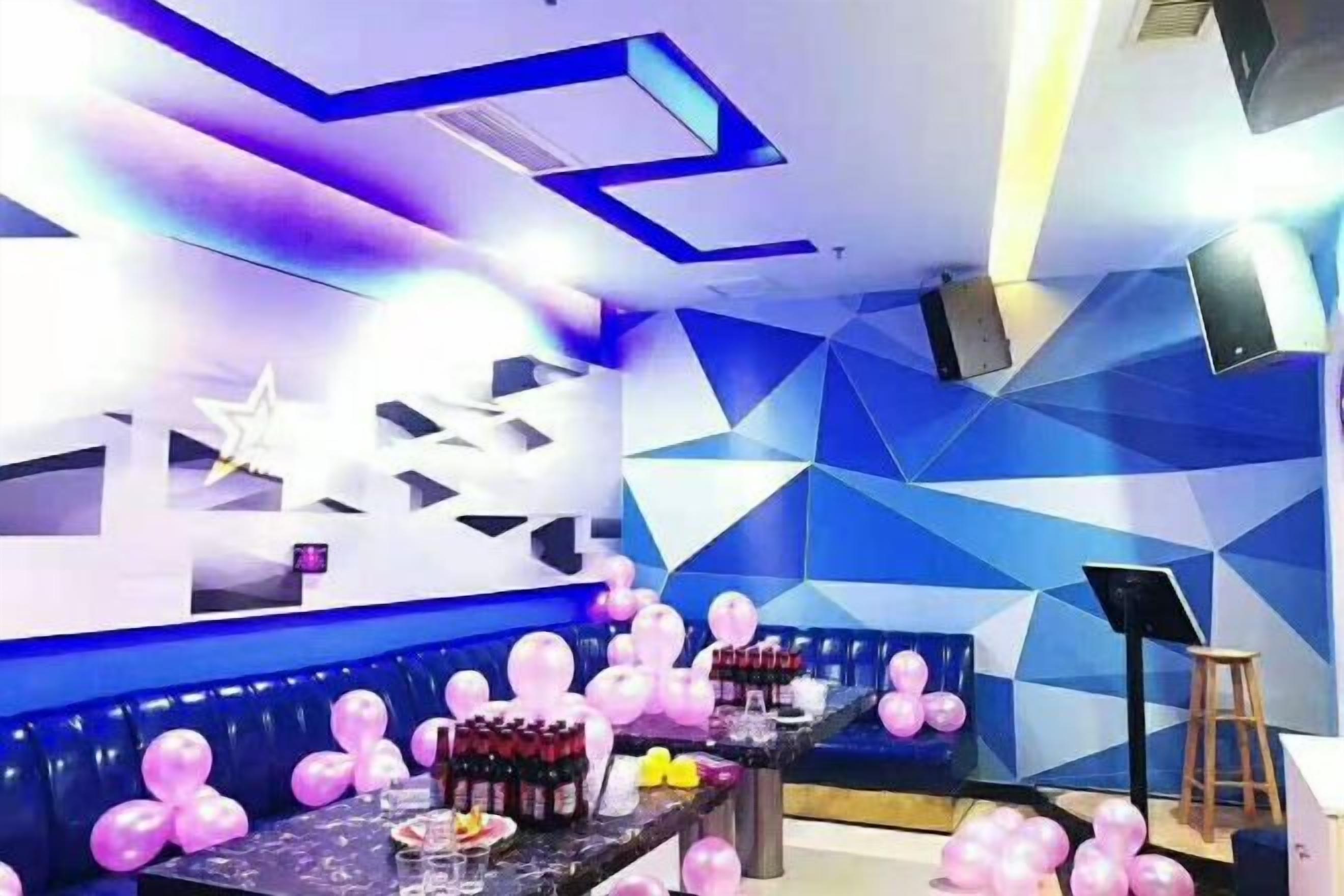 A room with a geometric wall design, a seating area with pink balloons, and a table with various items.