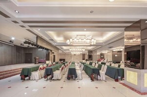 Un salón de banquetes con filas de mesas y sillas, un escenario y una zona de recepción.