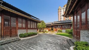 A courtyard with traditional wooden buildings, stone flooring, and a small garden area. - Fortune Hotel (Mangshi)