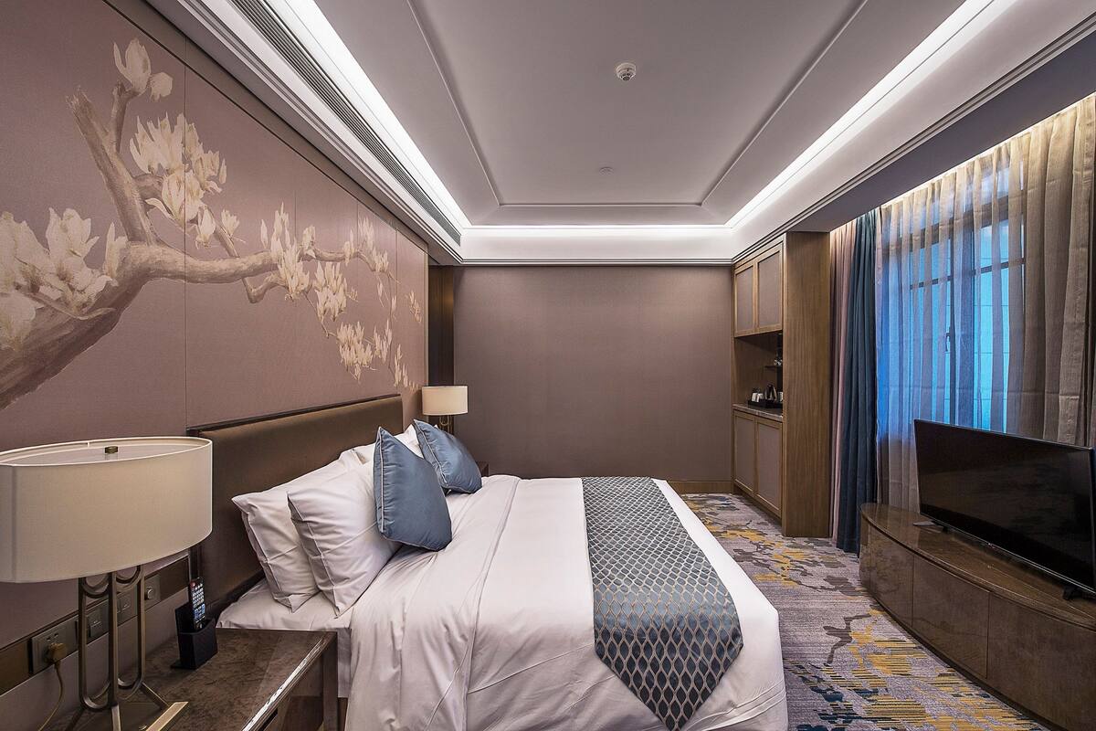 A hotel room with a large bed, a TV, a lamp, and a wall with a floral mural.