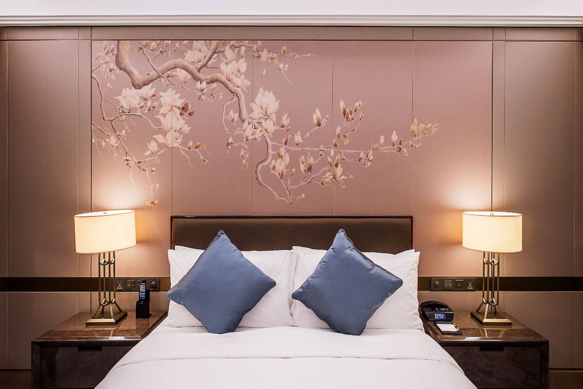 A hotel room with a large bed, two bedside tables with lamps, and a wall-mounted artwork depicting a tree with flowers.