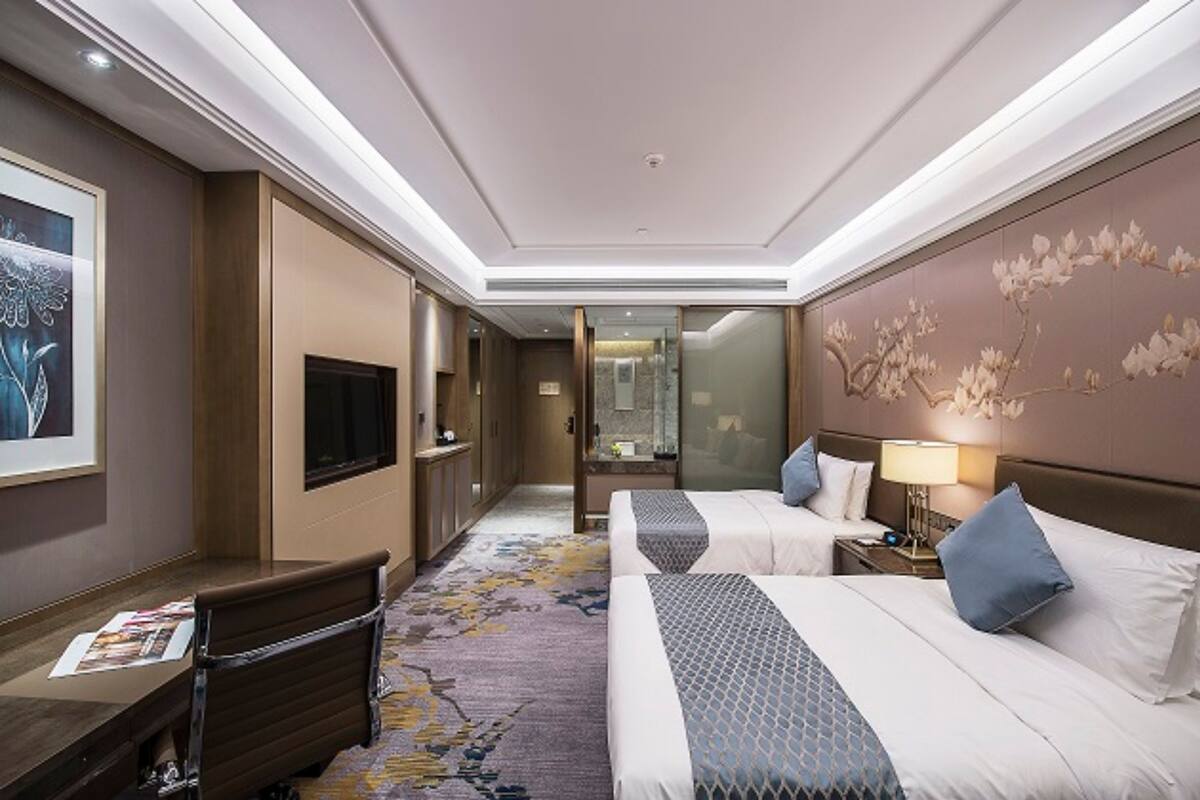 A hotel room with two beds, a desk, a TV, and a bathroom visible through a glass door.