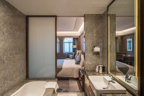 A modern hotel bathroom with a large mirror, two sinks, and a bathtub.