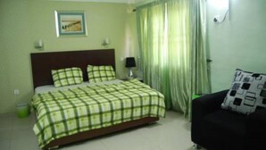 Un dormitorio con cama, mesita de noche, lámpara, sofá y ventana con cortinas.
