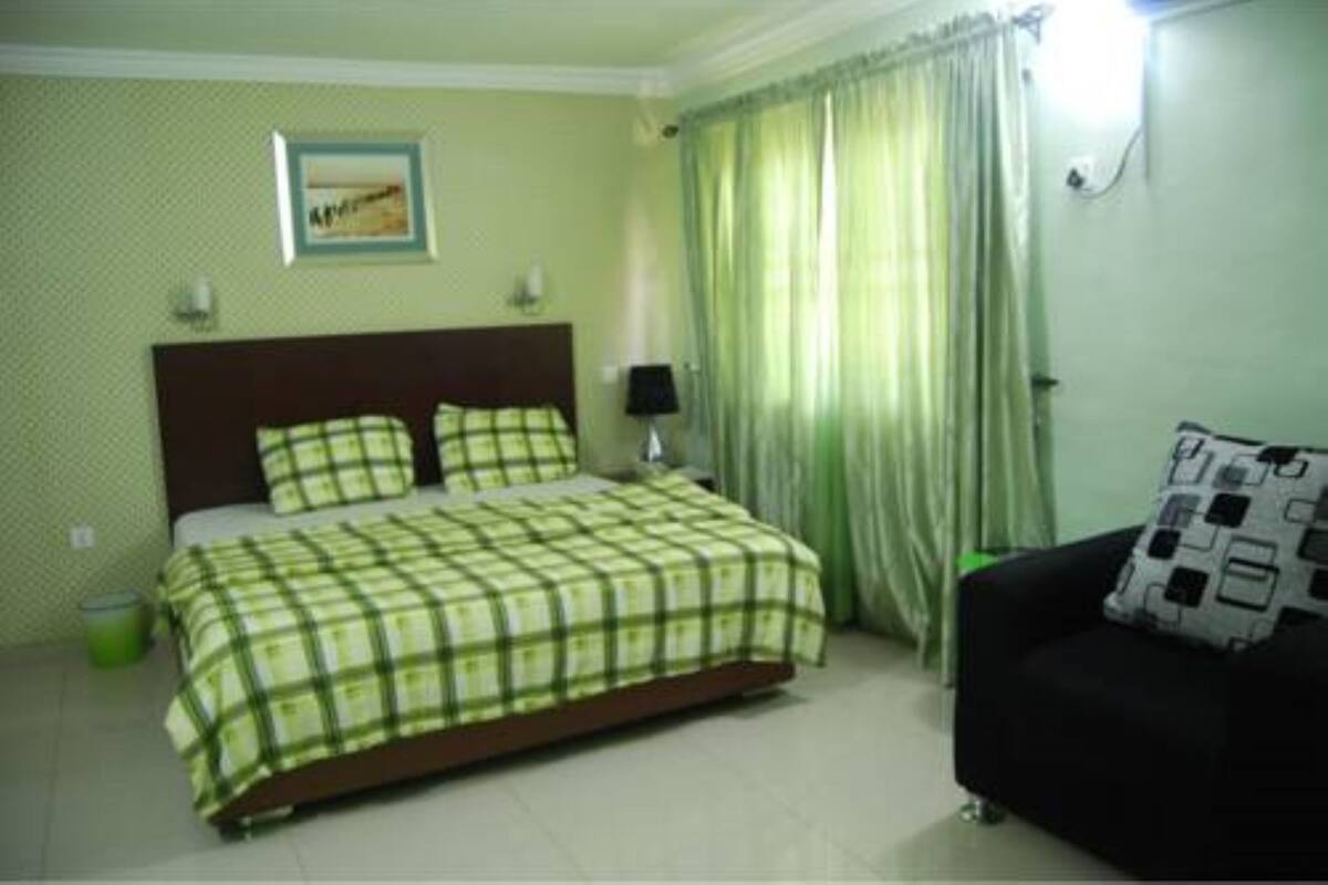 A bedroom with a bed, a nightstand, a lamp, a sofa, and a window with curtains.