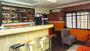 Zona de bar con mostrador, taburetes y televisor. Hay estantes con botellas y un ventanal con barrotes.
