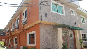 Un edificio de dos pisos con fachada de piedra y techo plano. Cuenta con múltiples ventanas con marcos blancos y un acceso nivelado con toldo verde.