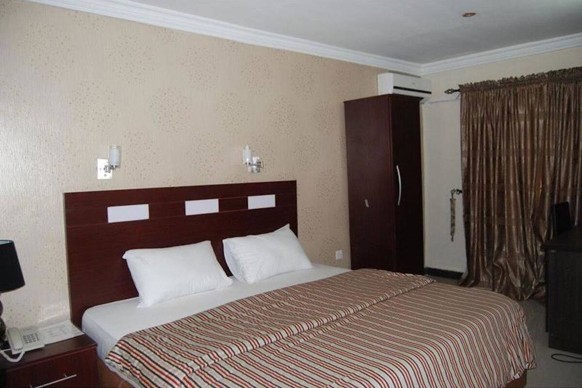 A hotel room with a large bed, a wardrobe, a bedside table with a lamp, and a door with curtains.