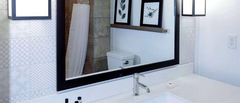 Un baño con lavamanos blanco, un espejo grande y cuadros en la pared.