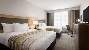 Une chambre d’hôtel avec deux lits, un bureau, une chaise, une télévision et une grande fenêtre avec des rideaux.