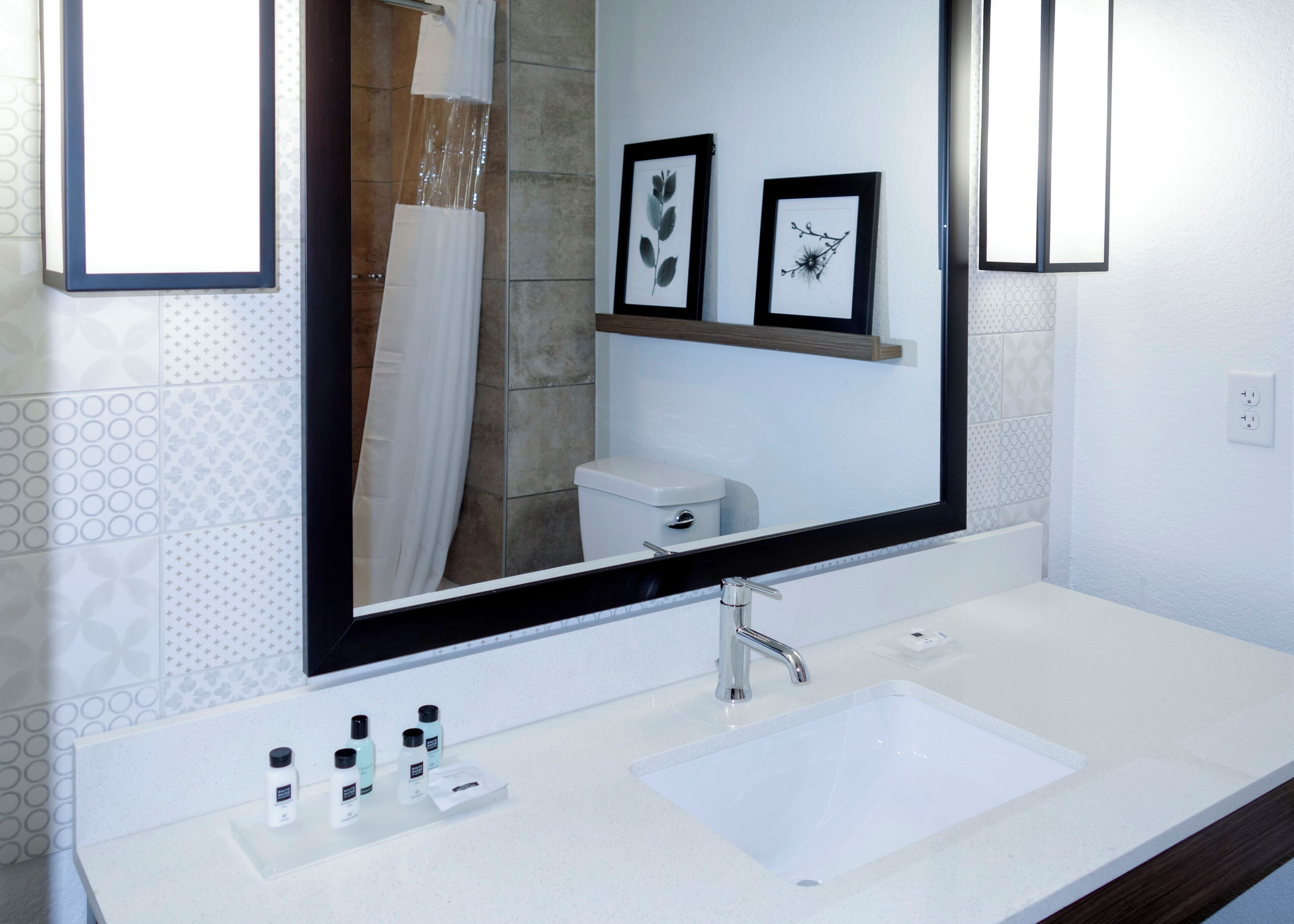 Baño con lavamanos blanco, espejo, cuadros enmarcados en la pared y cortina de ducha.