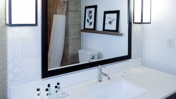 A bathroom with a white sink, a mirror, framed pictures on the wall, and a shower curtain.