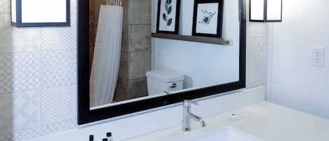 Baño con lavamanos blanco, espejo, cuadros enmarcados en la pared y cortina de ducha.