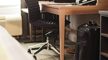 A hotel room with a wooden desk, a black office chair, a laptop, a telephone, and a black suitcase.