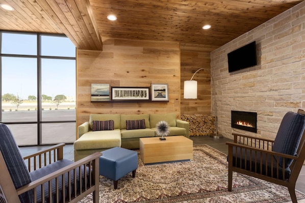 A cozy living room with a wooden ceiling, a fireplace, a large window, and a green sofa. - Country Inn & Suites by Radisson, New Braunfels, TX (New Braunfels)