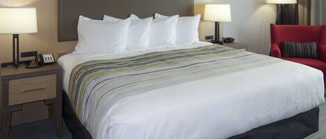 A hotel room with a large bed, two bedside tables with lamps, a red chair, and a nightstand with a phone.