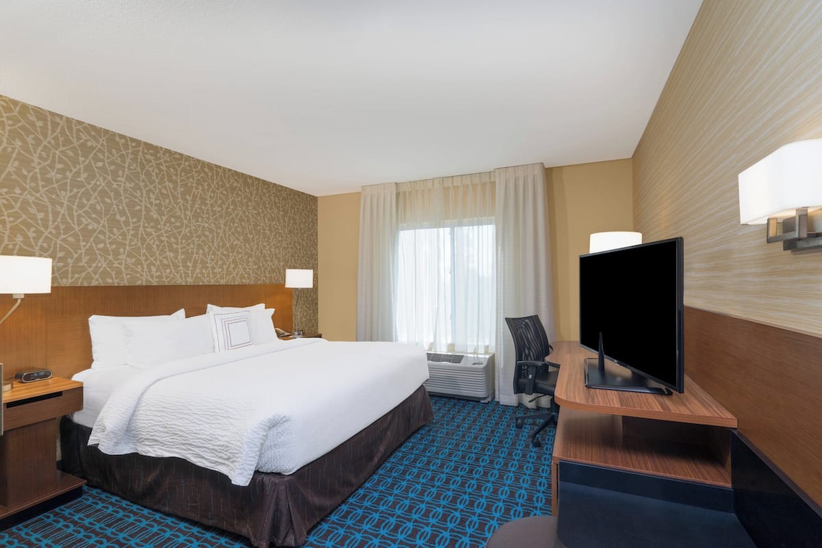 A hotel room with a large bed, a flat-screen TV, a desk, and a chair.