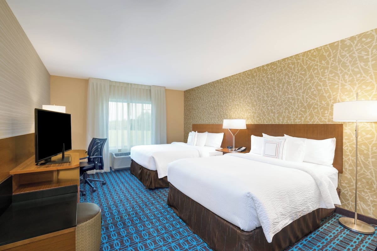 A hotel room with two beds, a desk with a TV, a chair, a lamp, and a patterned carpet.
