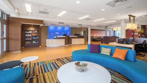 A modern hotel lobby with a reception desk, seating area, and a bookshelf. - Fairfield Inn & Suites by Marriott Bloomsburg (Bloomsburg)