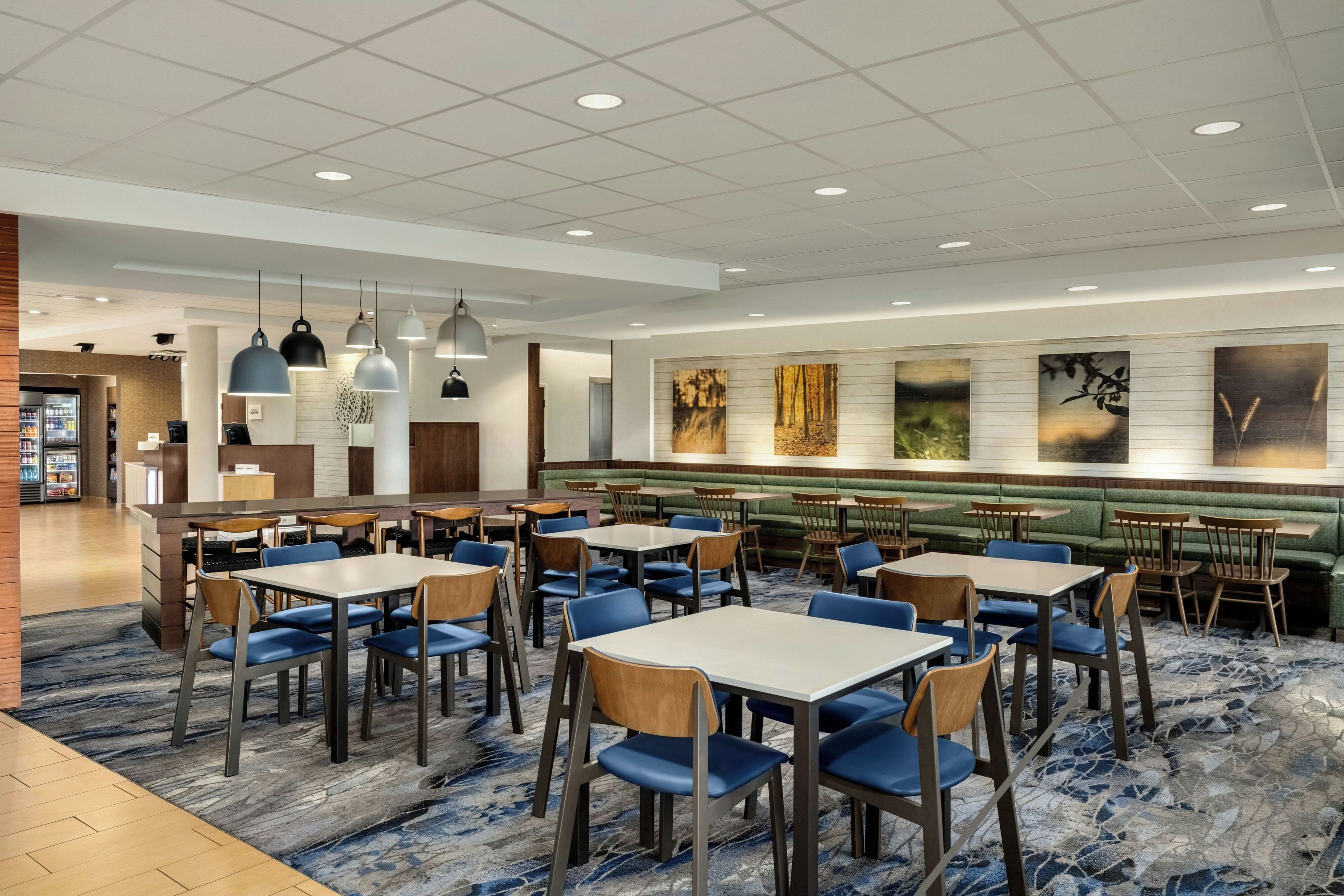 Un restaurant moderne doté de plusieurs espaces de restauration, notamment des banquettes et des tables, ainsi que de différents types de luminaires au plafond.