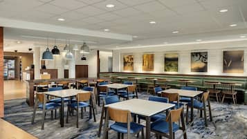 A modern restaurant with multiple dining areas, including booths and tables, and a variety of ceiling lights.