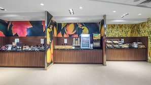 A reception area with a wooden counter, a self-service beverage station, and a wall with a fruit-themed mural. - Fairfield Inn & Suites by Marriott Bloomsburg (Bloomsburg)