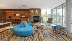 A modern lobby with a stone fireplace, a reception desk, and a seating area with a blue sofa and ottoman. - Fairfield Inn & Suites by Marriott Bloomsburg (Bloomsburg)