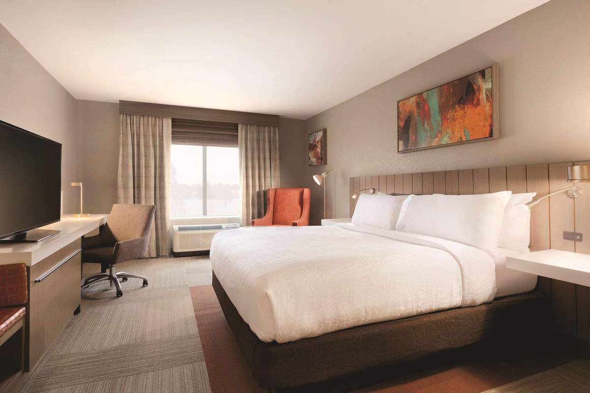 A hotel room with a large bed, a desk with a chair, a television, and a painting on the wall.