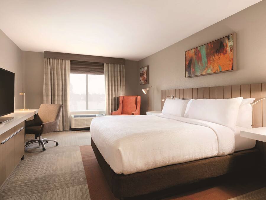 Une chambre d’hôtel avec un grand lit, un bureau avec une chaise, une télévision et un tableau au mur.