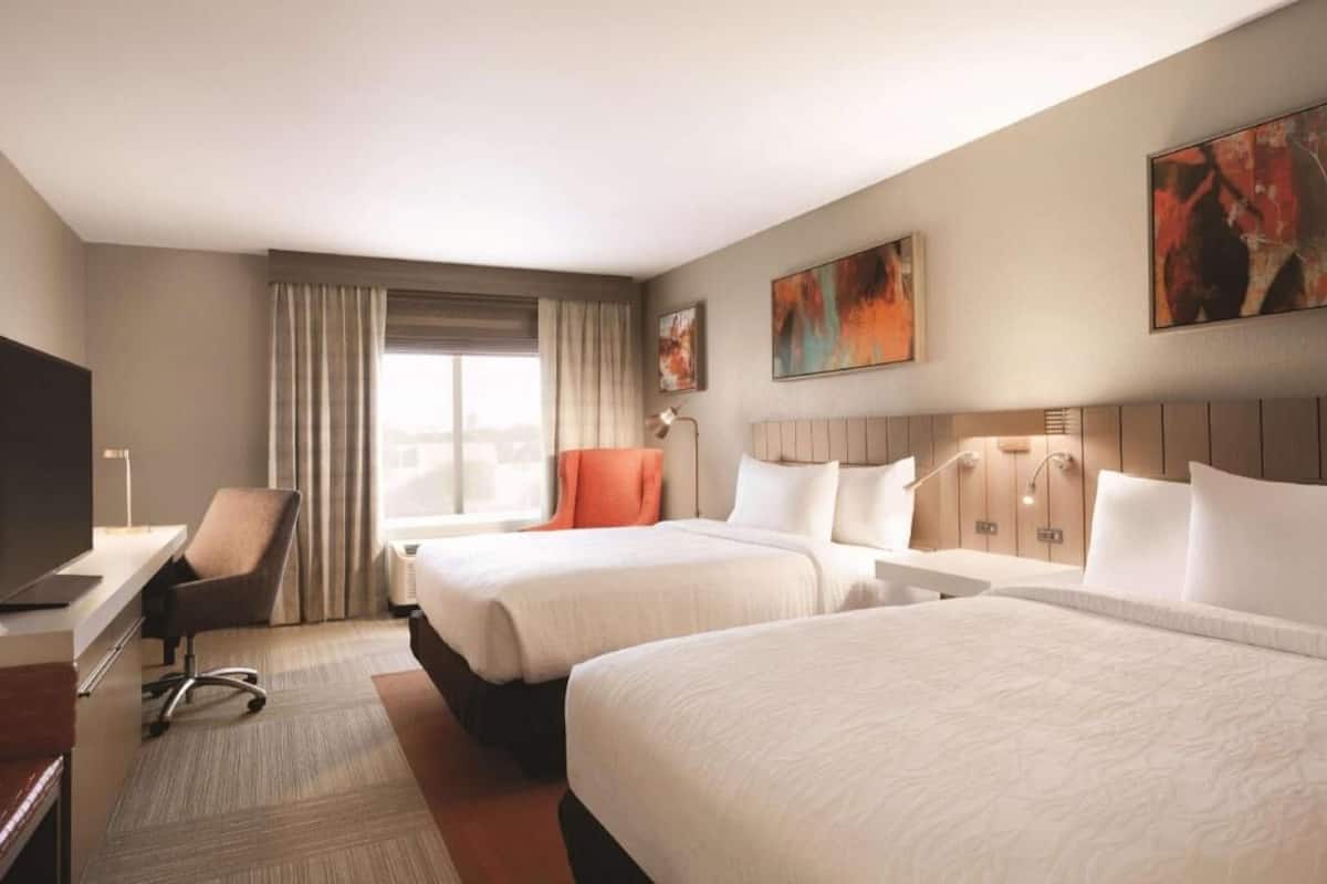 A hotel room with two beds, a desk, a chair, and artwork on the walls.