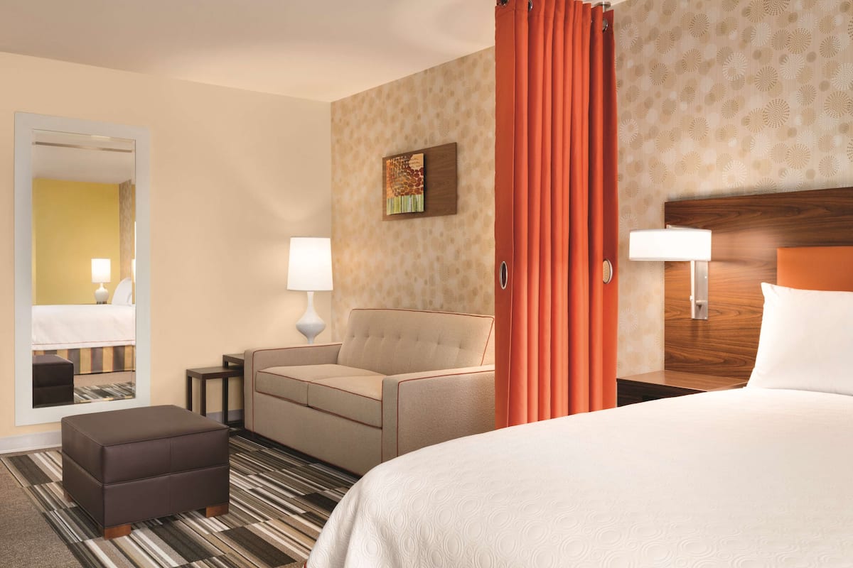 A hotel room with a bed, a sofa, a small table, a lamp, and a mirror.
