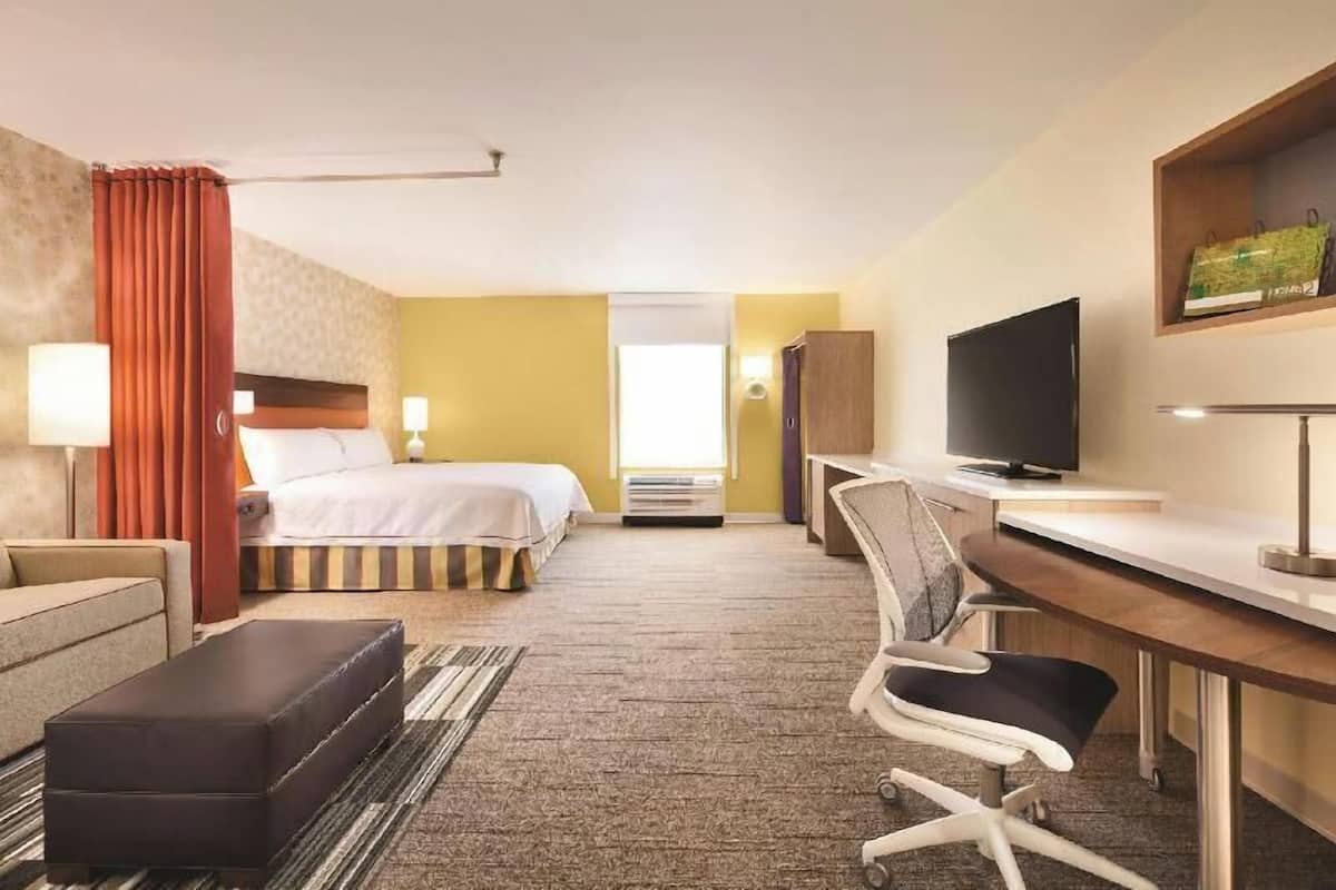 A hotel room with a bed, a desk, a chair, a television, and a sofa.