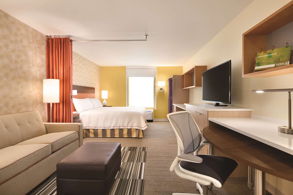 A hotel room with a bed, a sofa, a desk, a chair, a television, and a lamp.