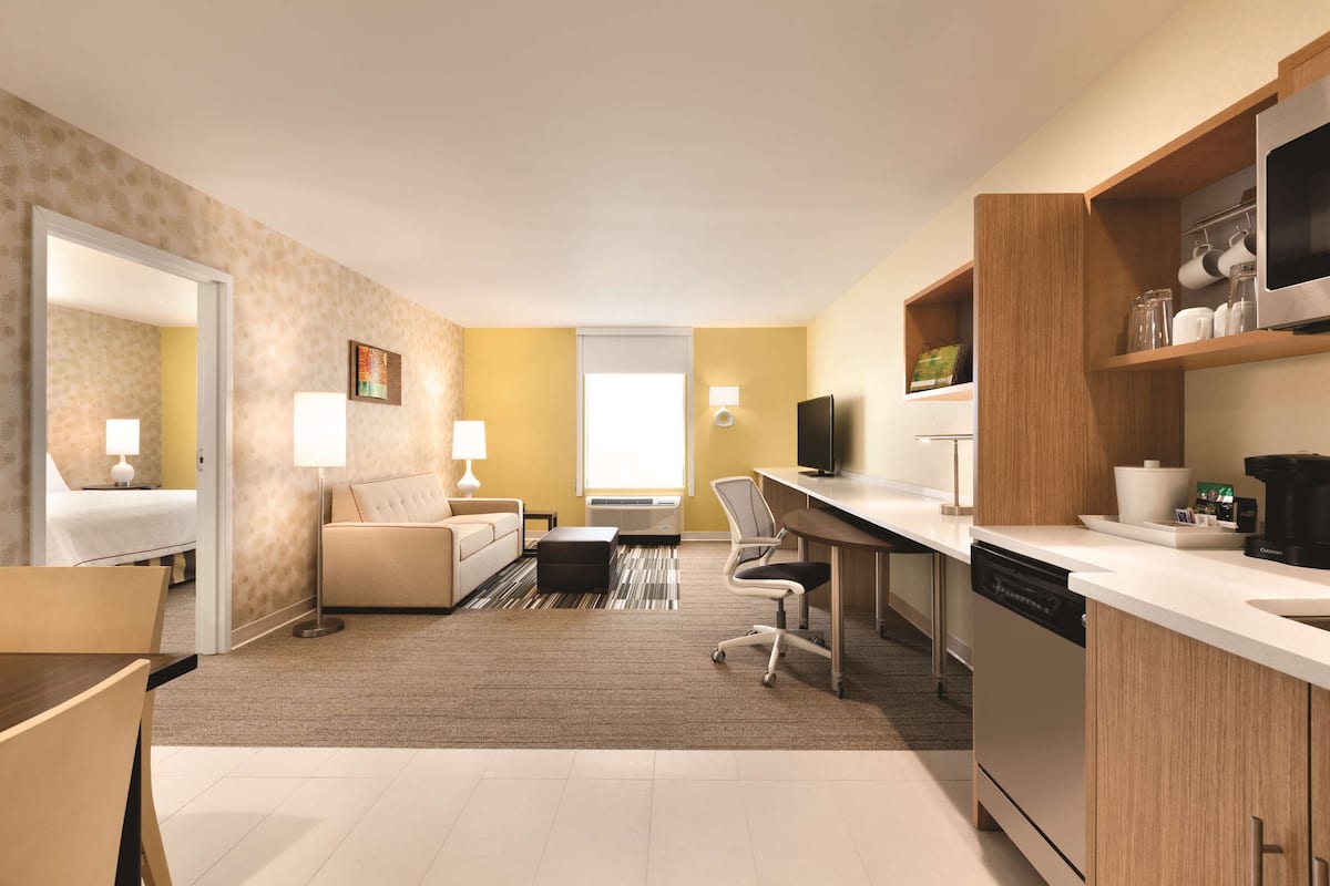A modern hotel room with a living area, a kitchen, a dining area, and a separate bedroom.